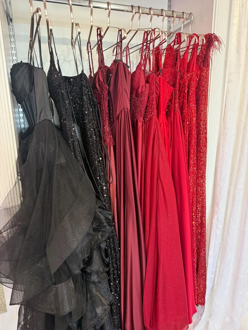 Black sequinned and ruffled prom gowns hanging next to a run of scarlet, crimson and burgundy dresses in satin, sequin and feather trim