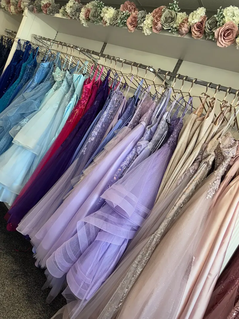 Prom gowns on the boutique rail in cobalt and turquoise beside fuchsia, deep purple, lilac and champagne, several with beaded and appliquéd bodices