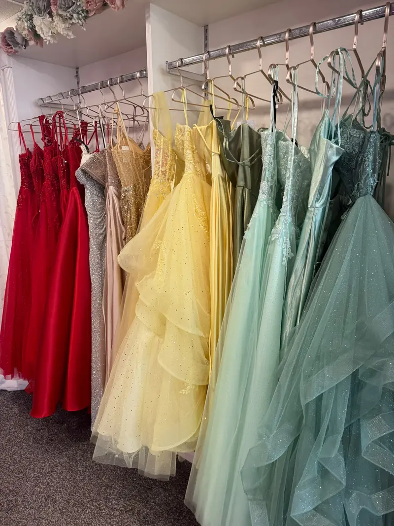 Prom dresses on a boutique rail in red, silver, champagne, buttercup yellow, sage and mint green
